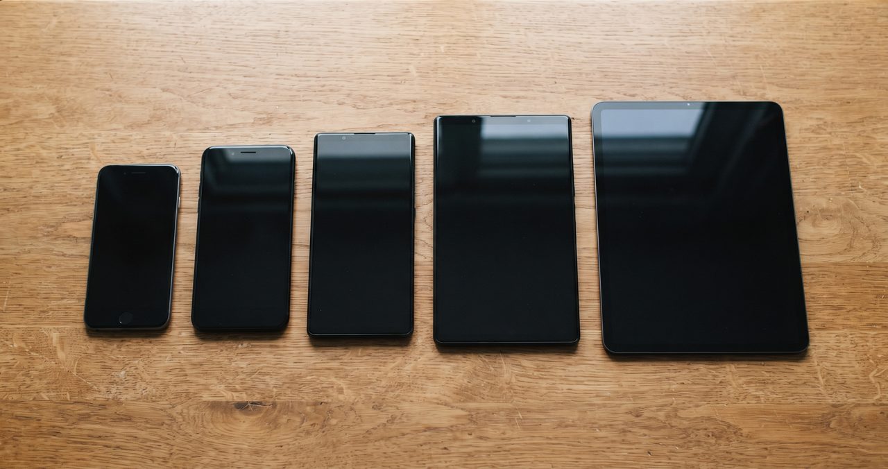 電源オフの状態のスマートフォンとタブレット4台をテーブルに並べて撮影した写真、家族の複数端末をまとめてセキュリティ対策するイメージ